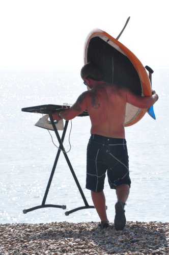 Man carrying a ironing board and paddle board to the seafront.